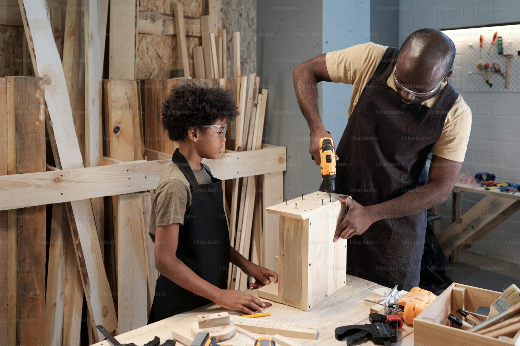 A man and a young apprentice building a wooden project together in a workshop