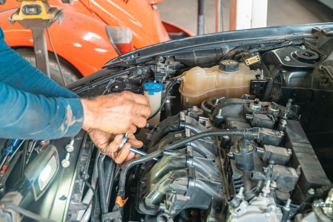 A man working on a car engine under the raised hood in a garage