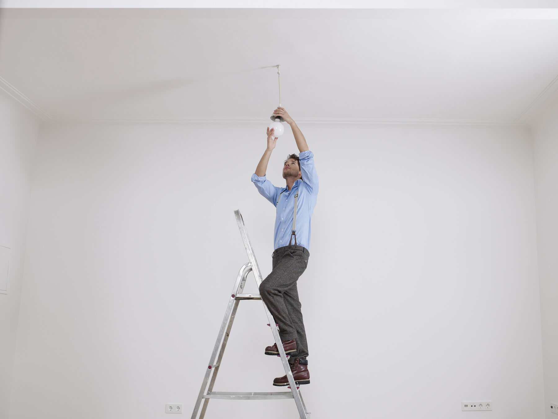 A man on a stepladder installing a ceiling light fixture