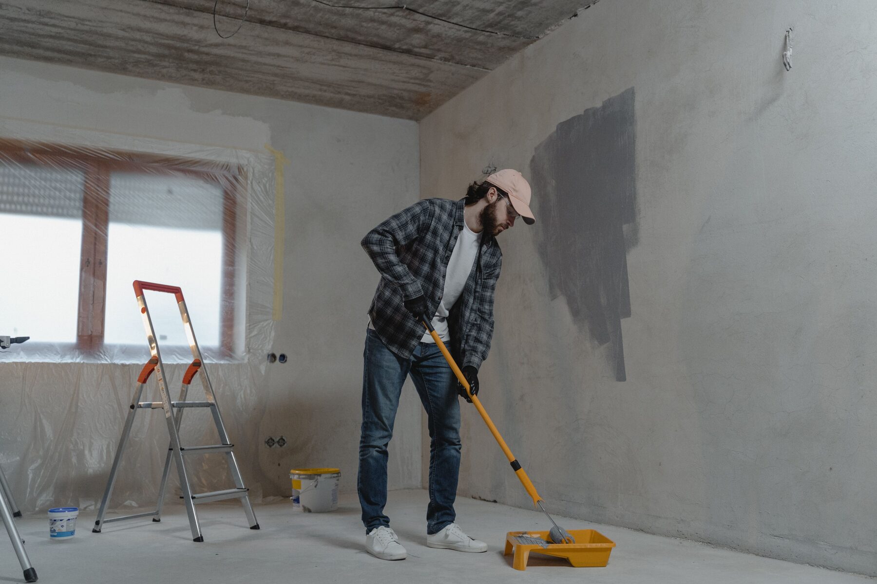 A man in a plaid shirt rolling paint onto a freshly prepared interior wall