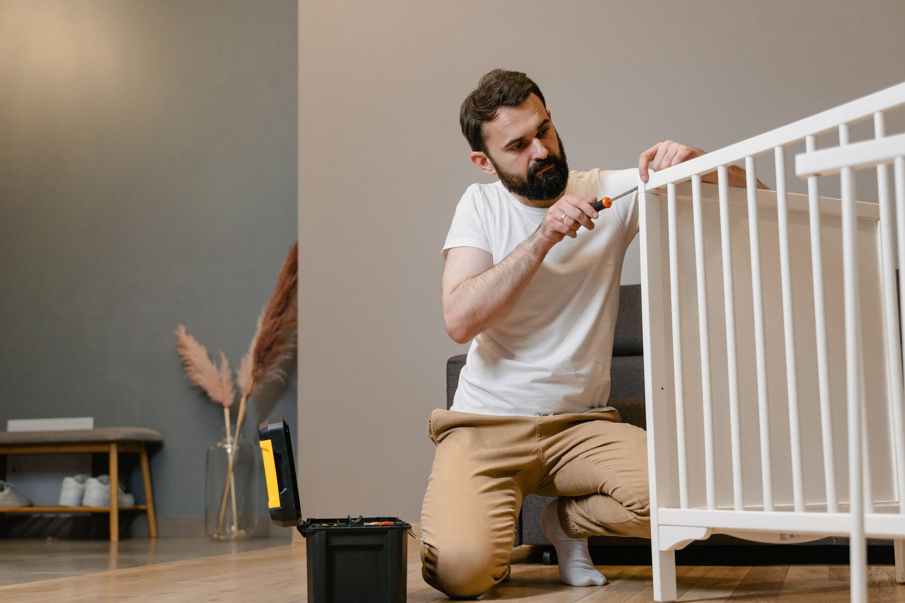 A man kneeling on the floor assembling flat-pack furniture with a screwdriver